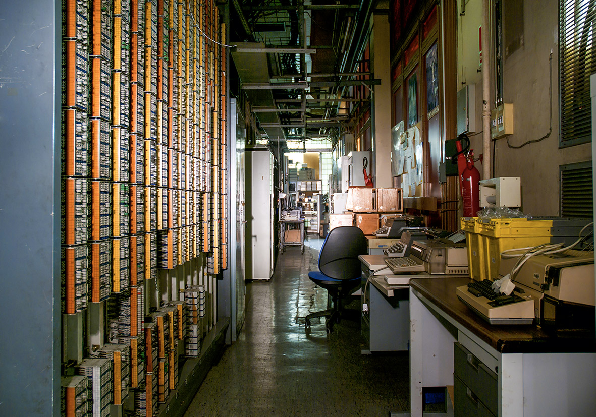 Pasillo de un laboratorio con un escritorio, paneles eléctricos y una persona trabajando.