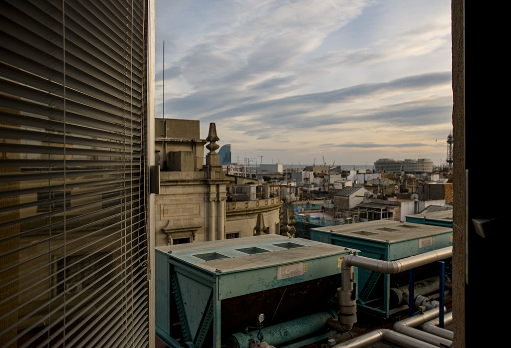 Vista urbana con nubes y edificios, con equipos de aire acondicionado en primer plano.