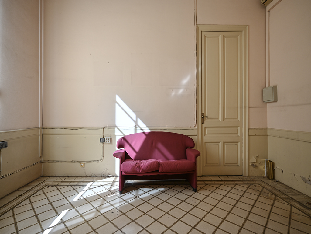 Sofá rojo en una habitación vacía con paredes rosadas y luz natural.