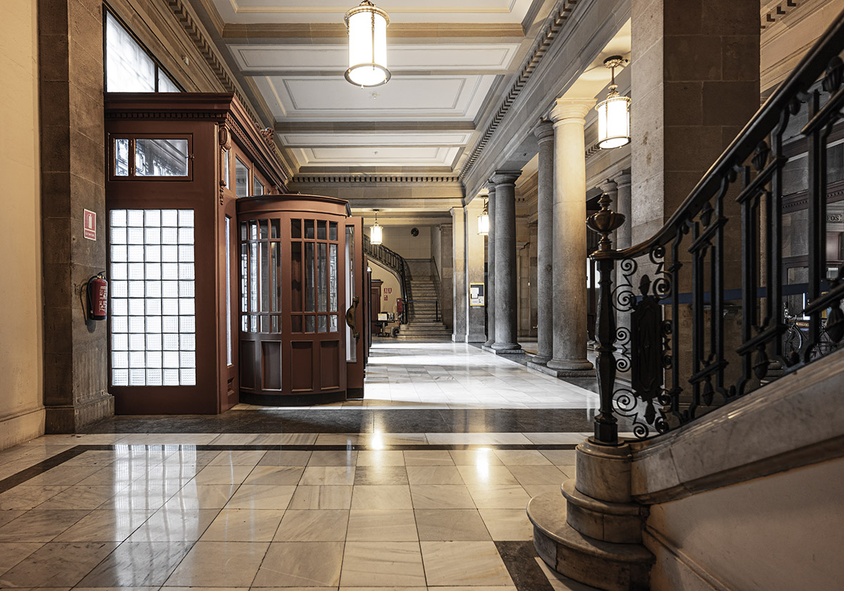 Vestíbulo elegante con escalera, cabina telefónica y luz natural.