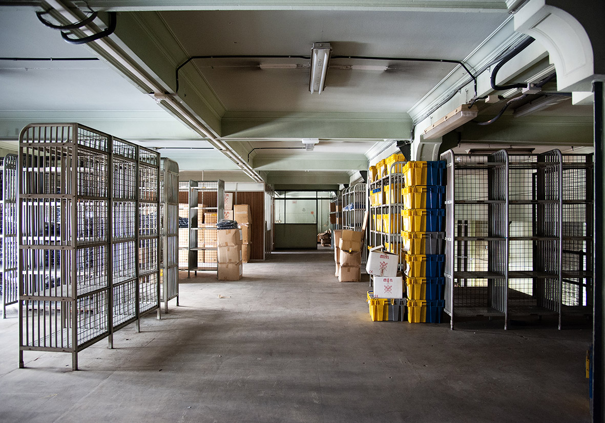 Interior de un almacén con estanterías metálicas y cajas apiladas. Iluminación natural.