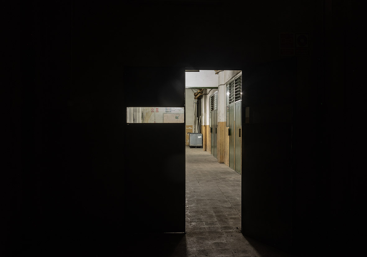 Puerta abierta en un pasillo oscuro con paredes de colores claros.