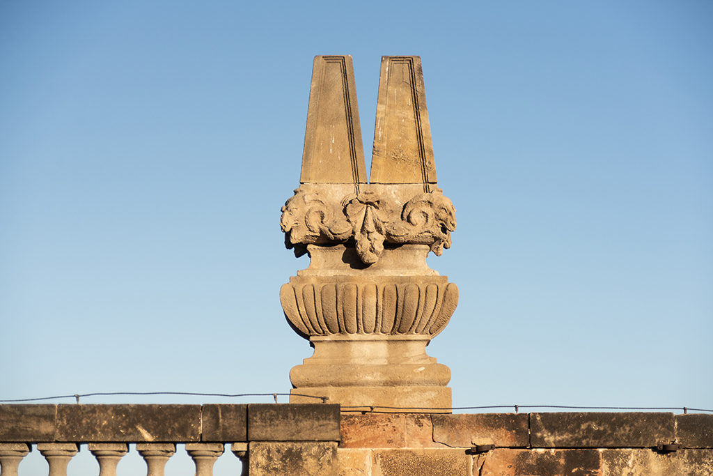 Adorno de piedra con forma de león sobre un pedestal, bajo un cielo azul.